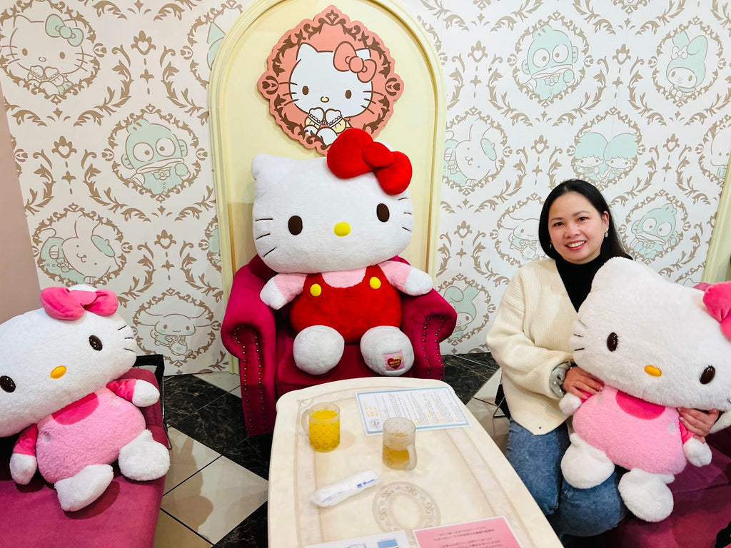 Lara posing with a life-sized Hello Kitty plush in a My Melody-themed seat at Sanrio Characters Garden Cafe Ueno, Tokyo.